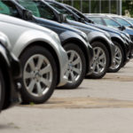 An angled side view of a row of parked cars. automotive stock picks